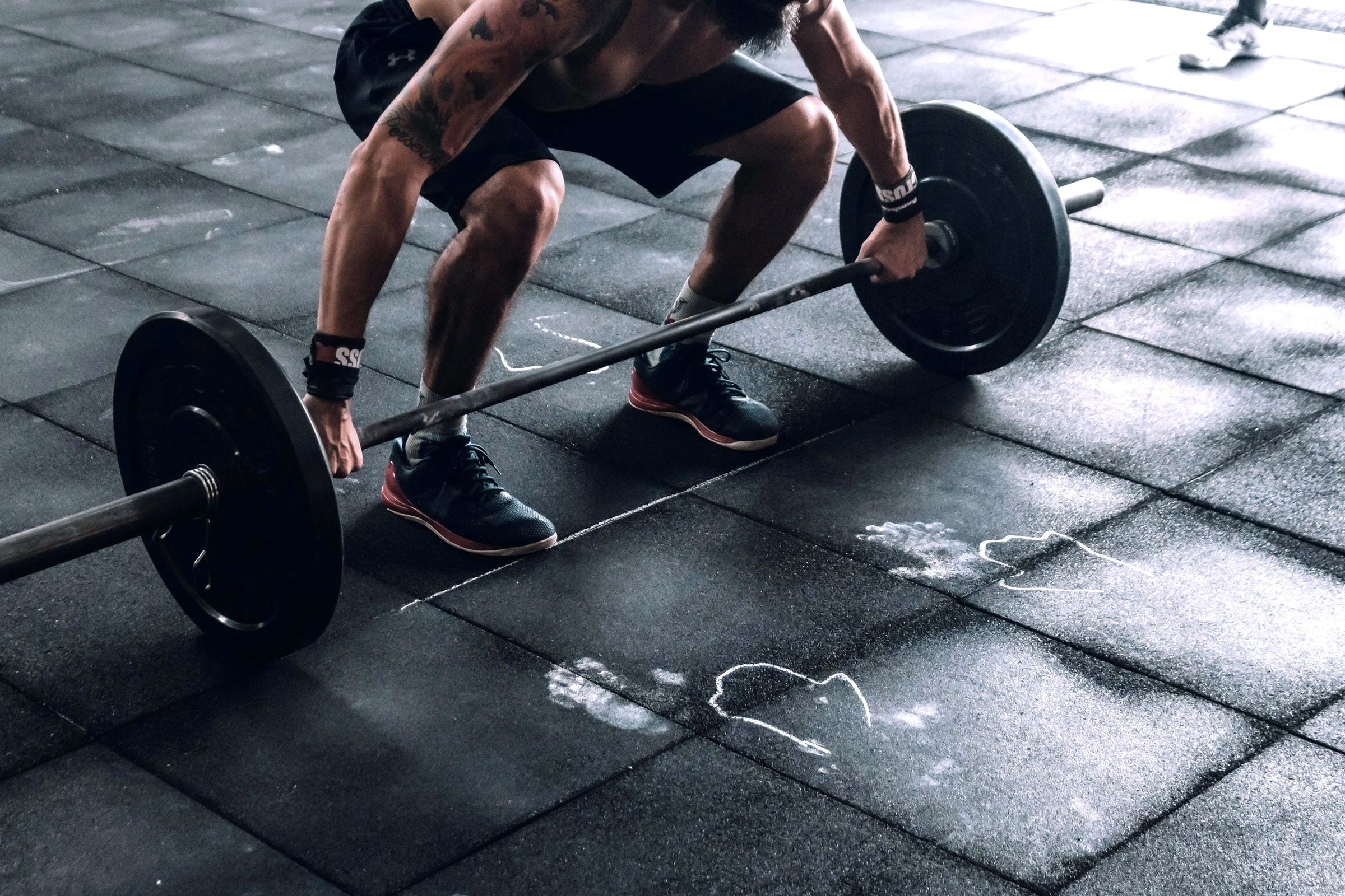 Chalked hands gripping a loaded barbell on a rubber gym floor