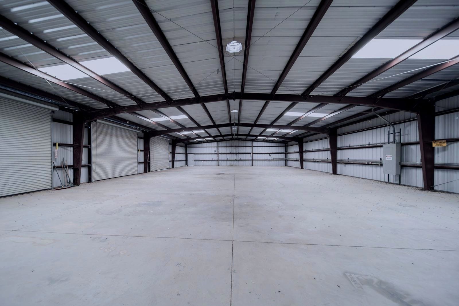 Empty industrial unit with roll-up doors, concrete floor and exposed steel frame.