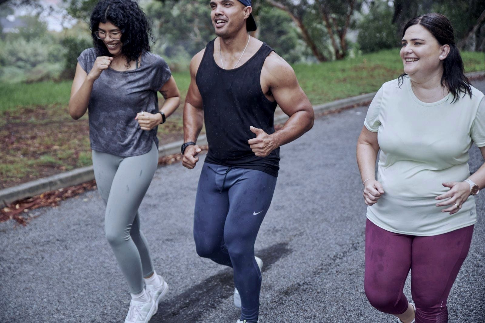 Three people running together on a tree-lined road, smiling and chatting.