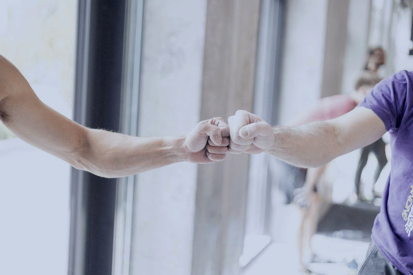 Two people bumping fists in a training space with natural light.