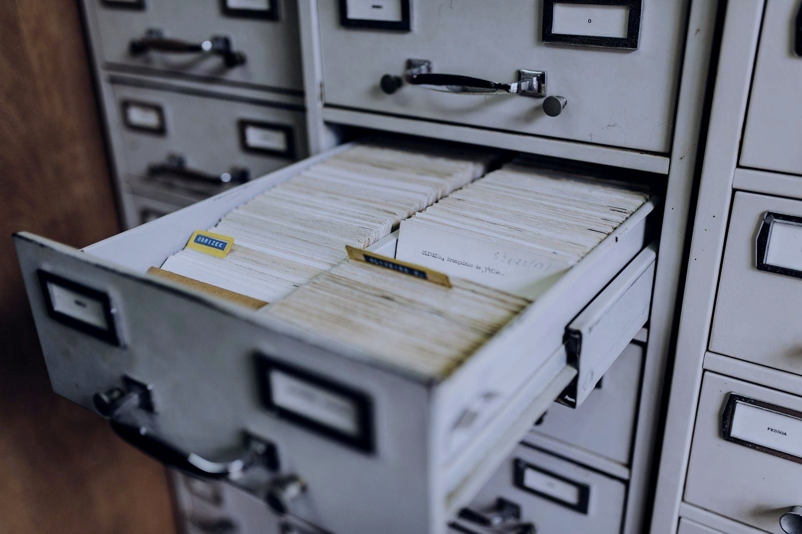 Open metal filing drawer full of paper index cards.