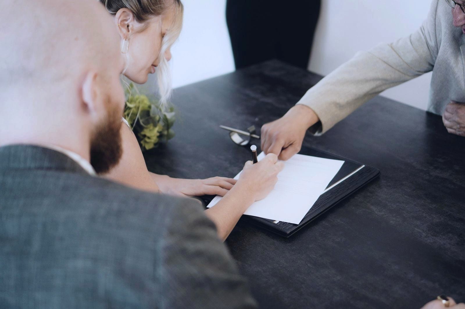 A person signing a document at a desk while another points to where to sign.